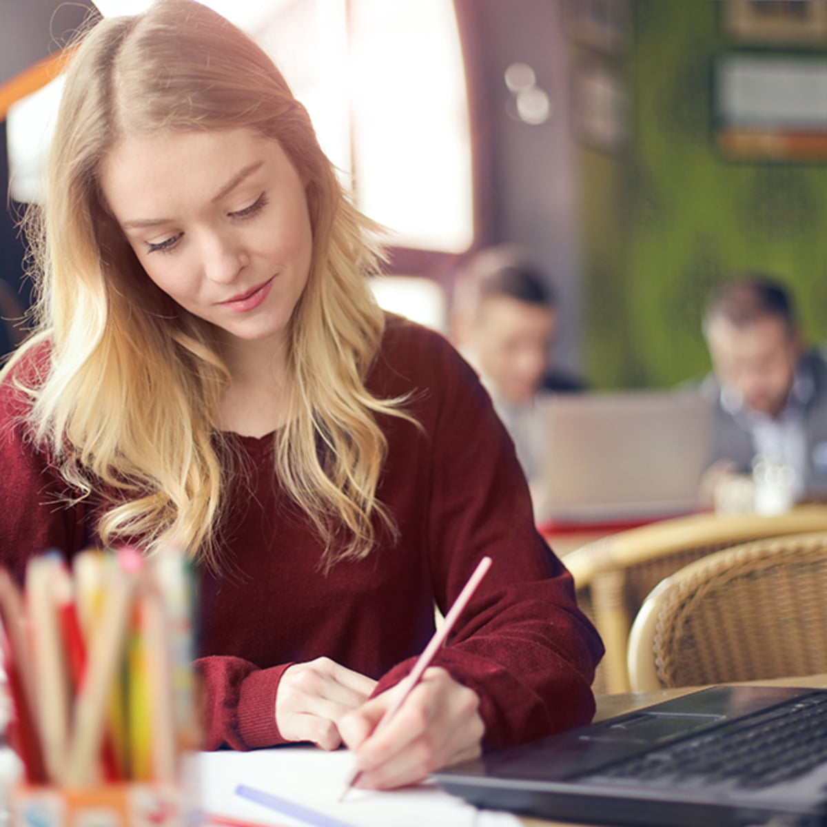 a young woman sitting at a table writing and working on her laptop computer