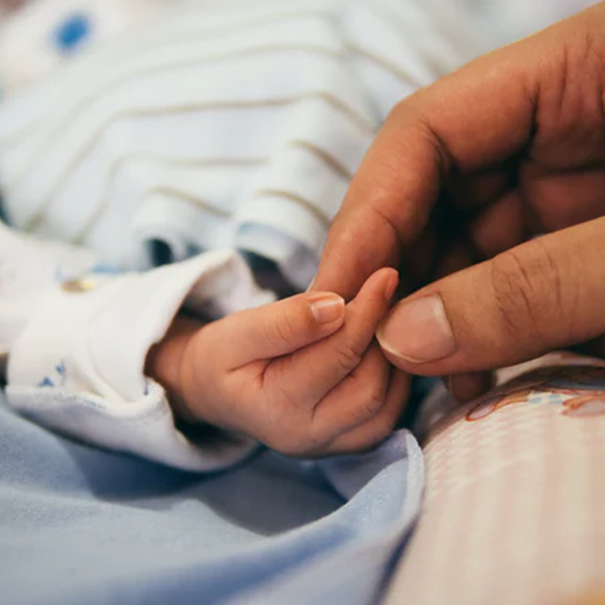 An adult hand holding a baby's hand